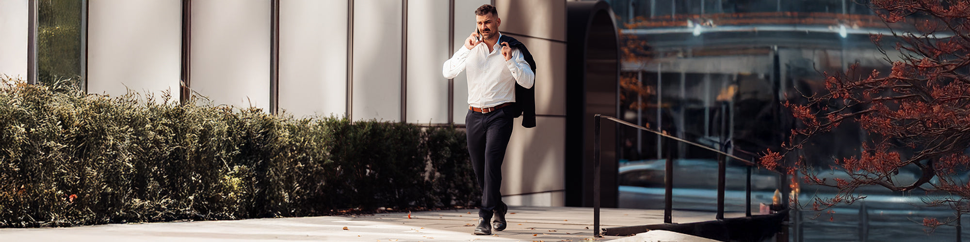 Un homme entre 25 et 40 ans marche avec un veston sur l'épaule, une chemise blanche uni et un pantalon propre