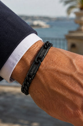 Bracelet chaîne noir porté au poignet avec plaques gravées Au Noir près d’un poignet de chemise pour homme, détail