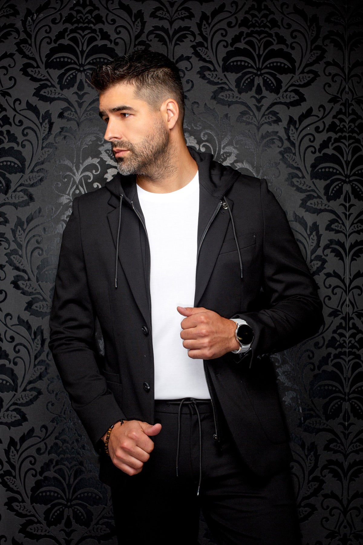 Men's black hooded blazer in angled model view, with zip insert, drawstrings, and notched lapels, side view by Au Noir