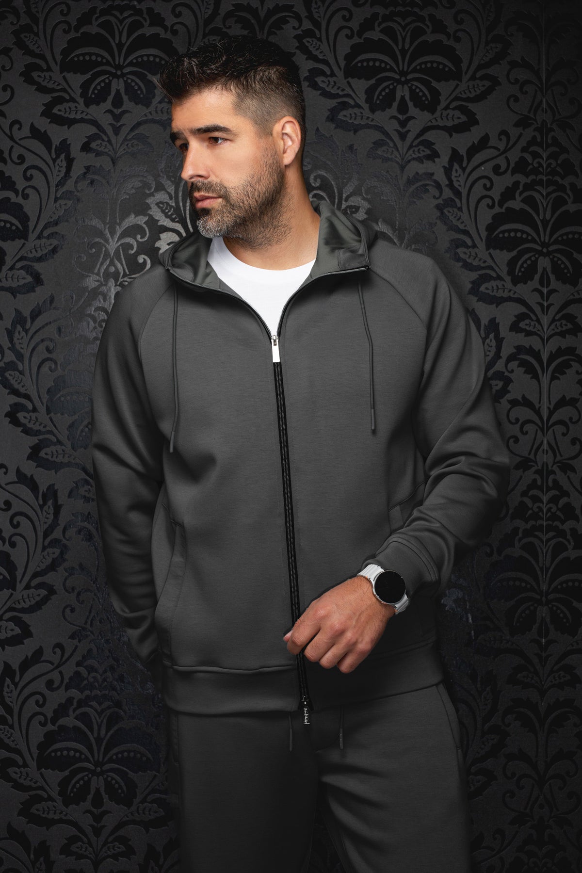 Men's dark gray hooded zip sport jacket on model, front view with black zipper, drawcords, and banded hem by Au Noir