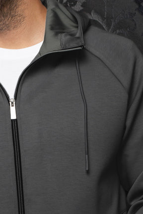 Au Noir men's dark gray hooded zip sport jacket showing black zipper, drawcord, raglan seam, and texture, close-up