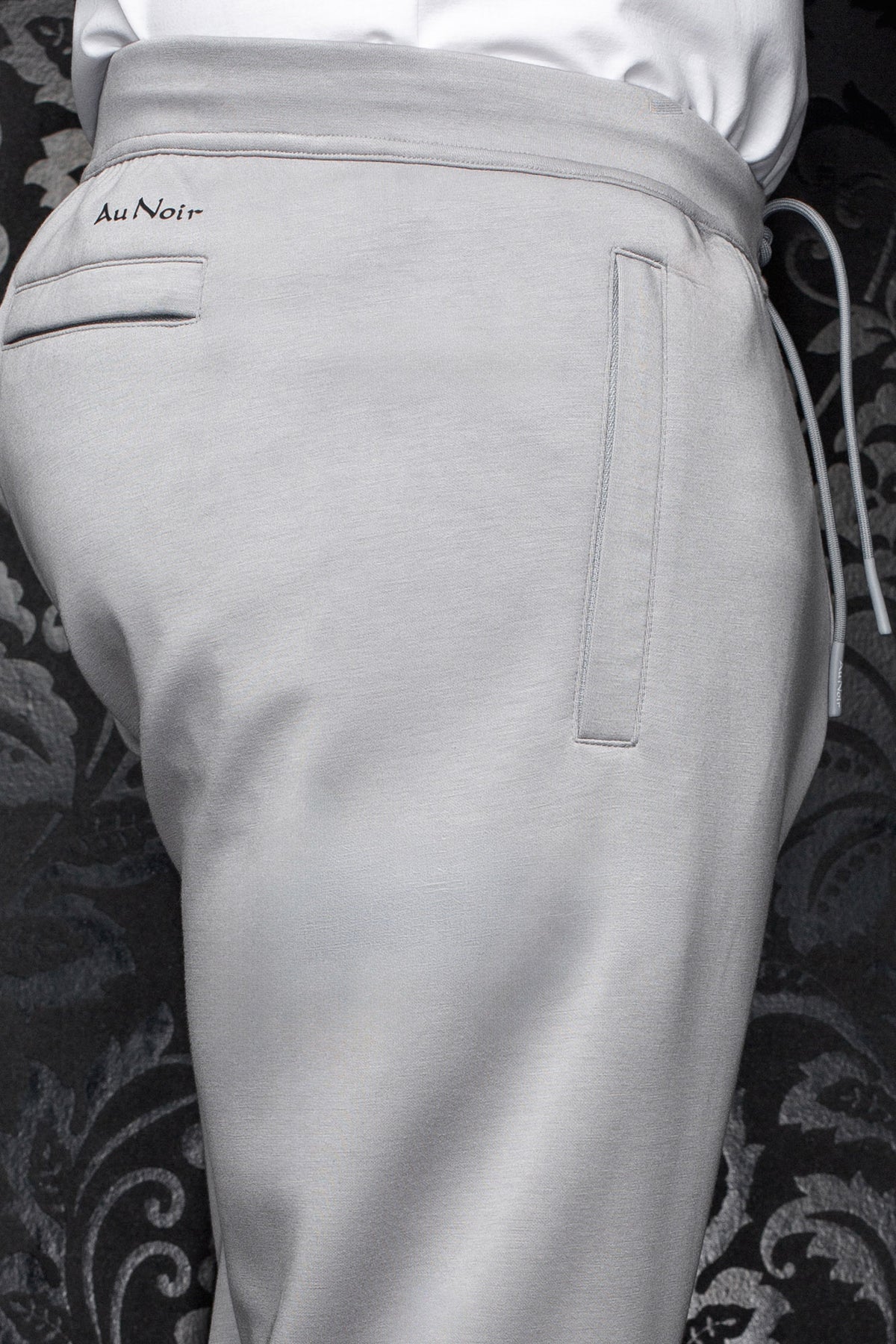 Men's light gray jogging pants waistband, drawcord, welt pockets, and small black Au Noir logo, close-up