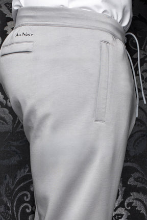 Men's light gray jogging pants waistband, drawcord, welt pockets, and small black Au Noir logo, close-up