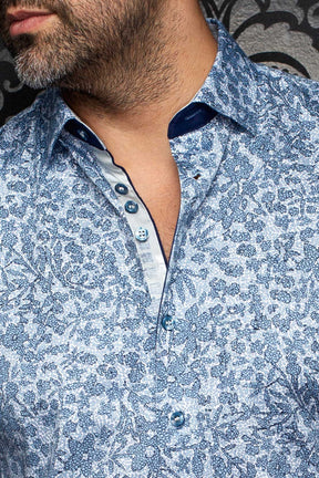 Gros plan du col, de la patte boutonnée et des garnitures marine d'une chemise fleurie bleue pour homme par Au Noir