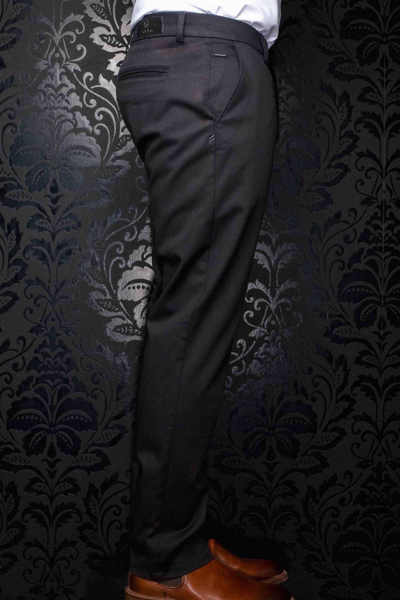 Men's side-back view of black chino pants on model with belt loops, rear pocket, and slim straight leg by Au Noir