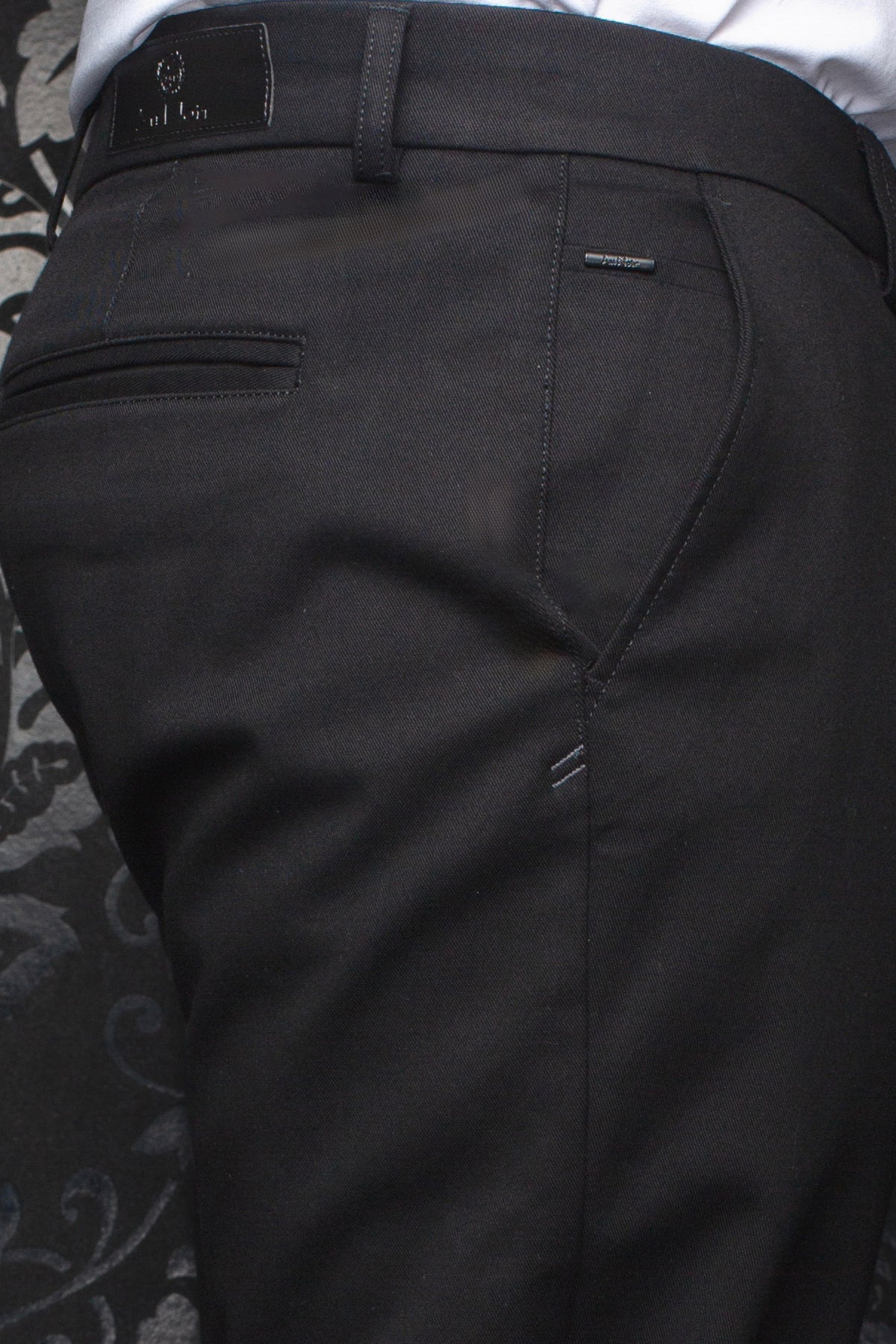 Au Noir men's black chino pants showing rear waistband, belt loop, welt pocket, and logo details, close-up