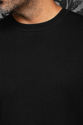 Au Noir men's black fine-knit crewneck cashmere sweater showing the ribbed collar and plain front, close-up