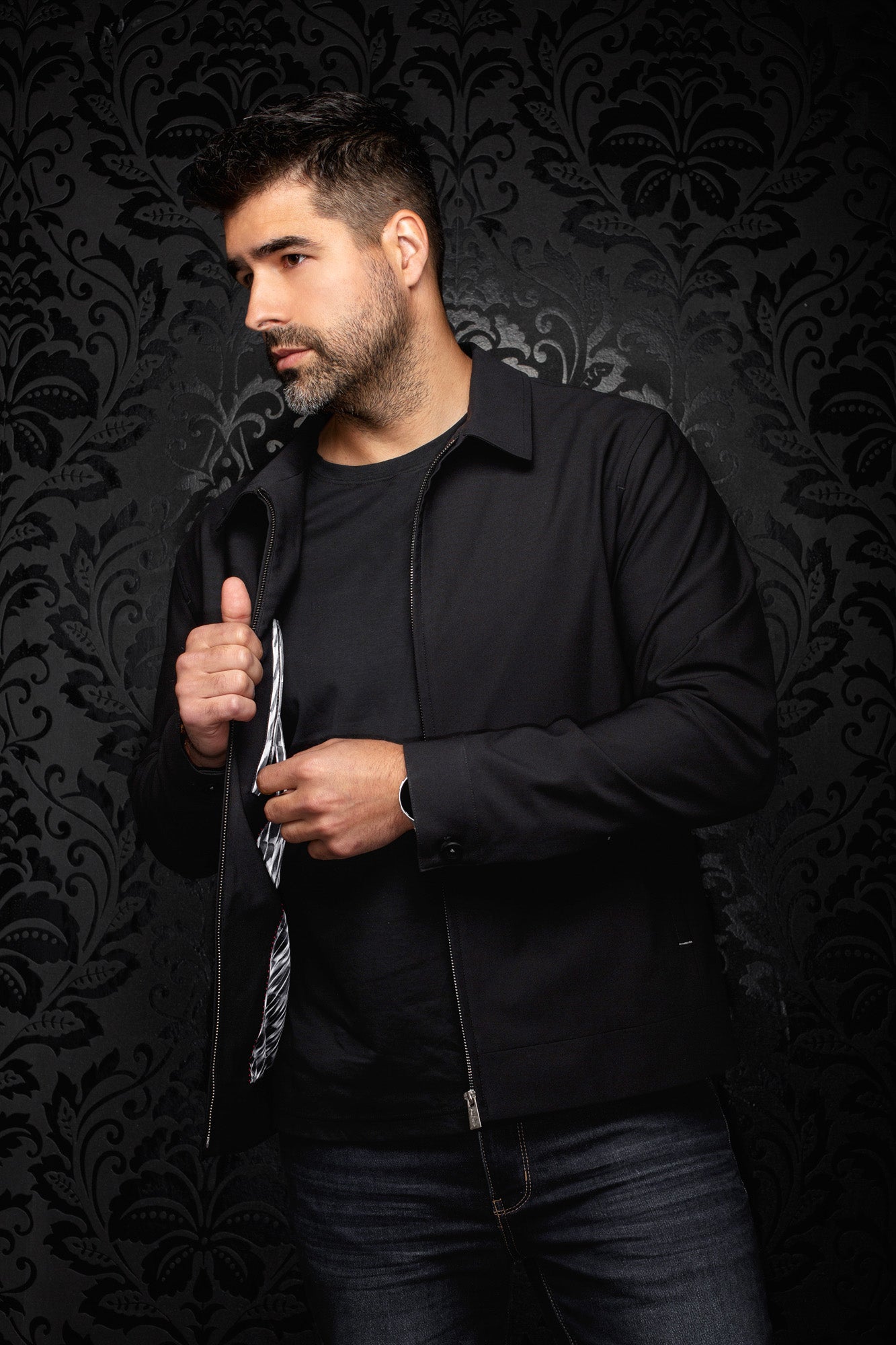 Men's angled view of a black zip bomber jacket opened to show a black-and-white patterned lining, side view by Au Noir