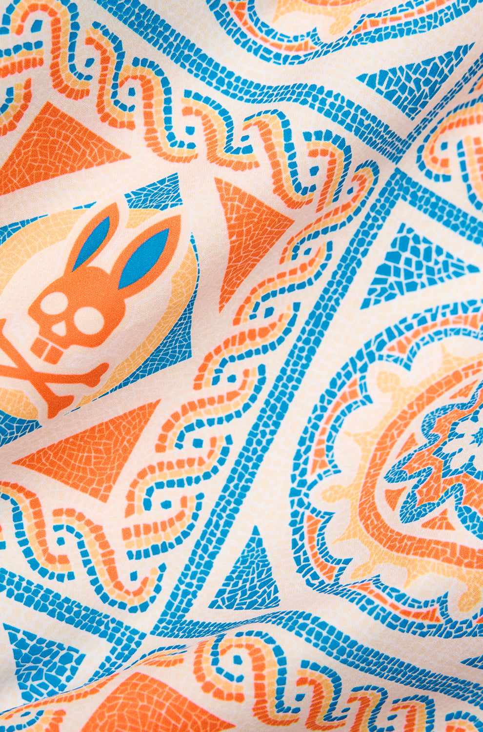 Psycho Bunny men's cream fabric with orange and blue mosaic tile print and bunny skull motif, close-up