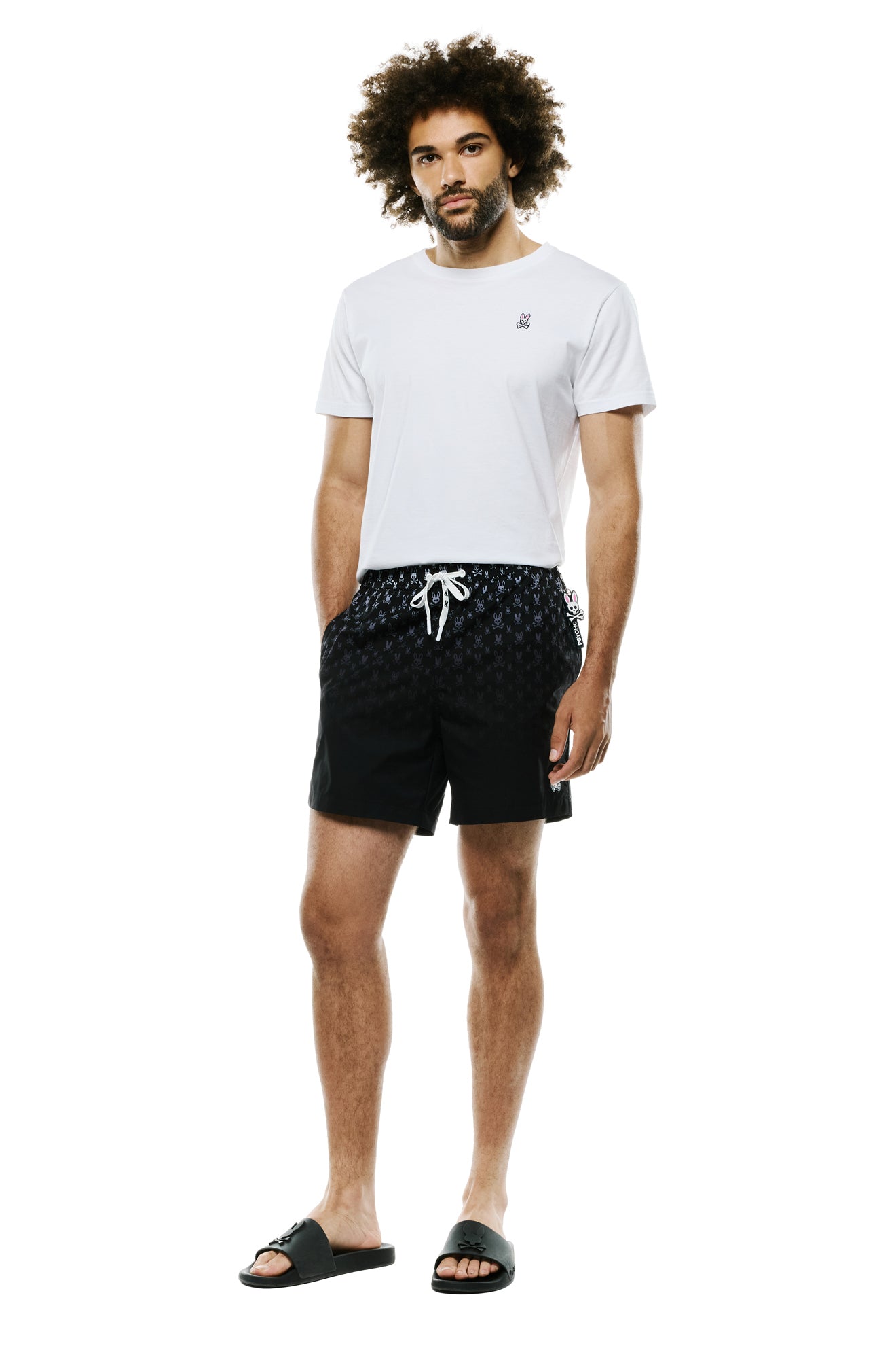 Men's full-body front view of black swim shorts with repeat bunny skull print and white drawstring by Psycho Bunny