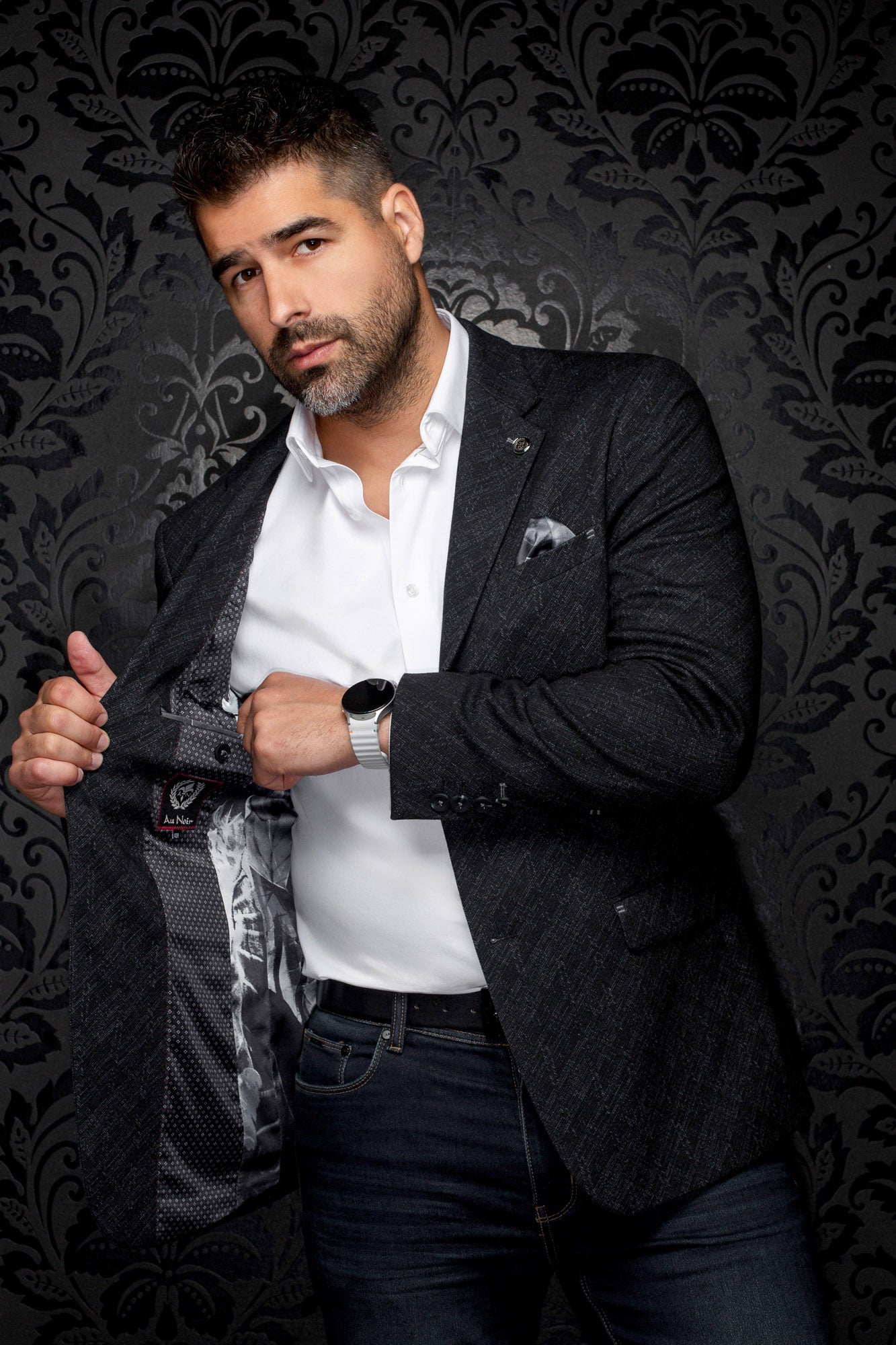 Men's angled view of a charcoal textured blazer opened to show dark patterned lining and logo label, detail view by Au Noir