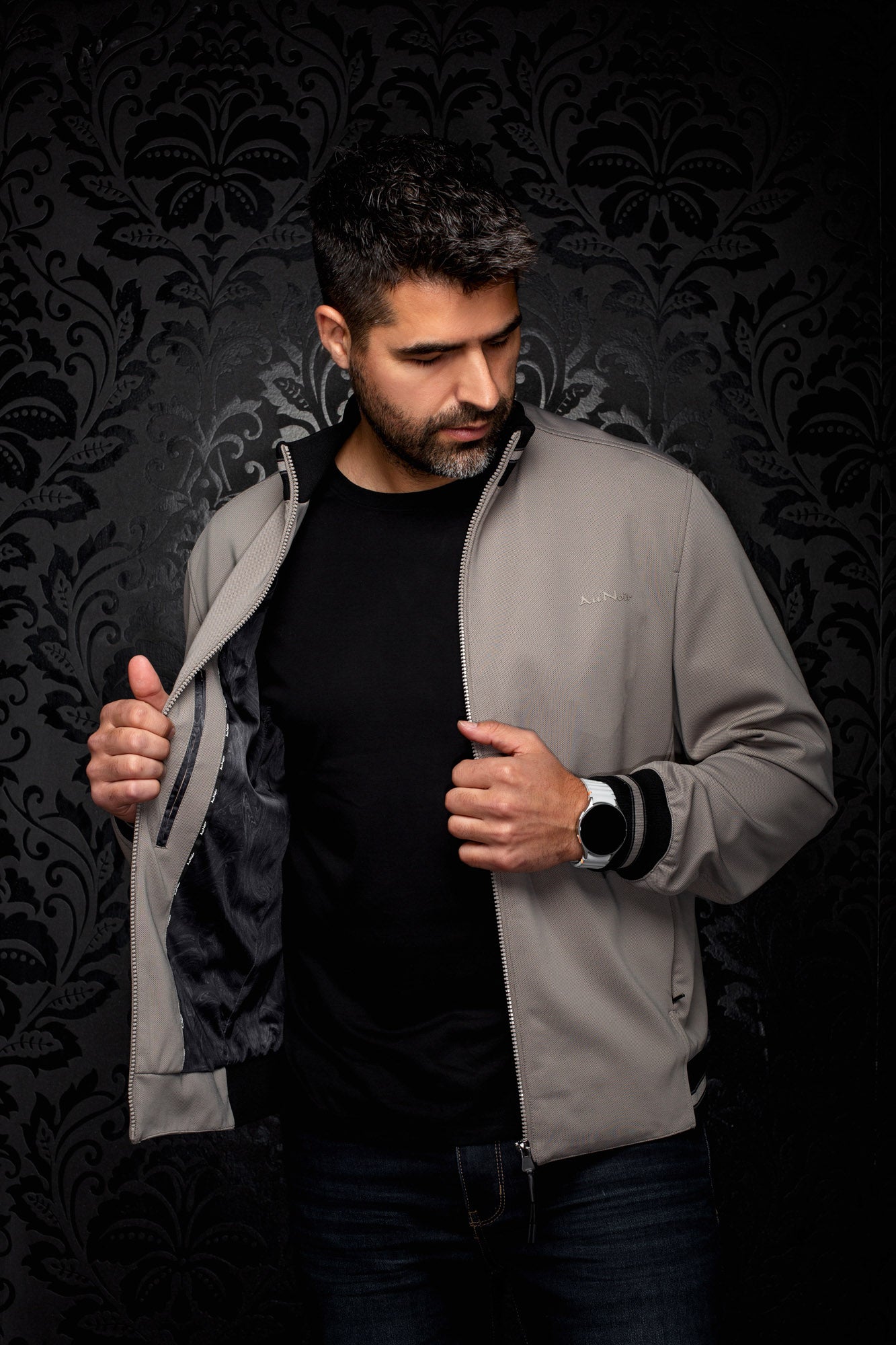 Au Noir men's gray bomber jacket held open to show black lining, front zipper, and small chest logo, detail view