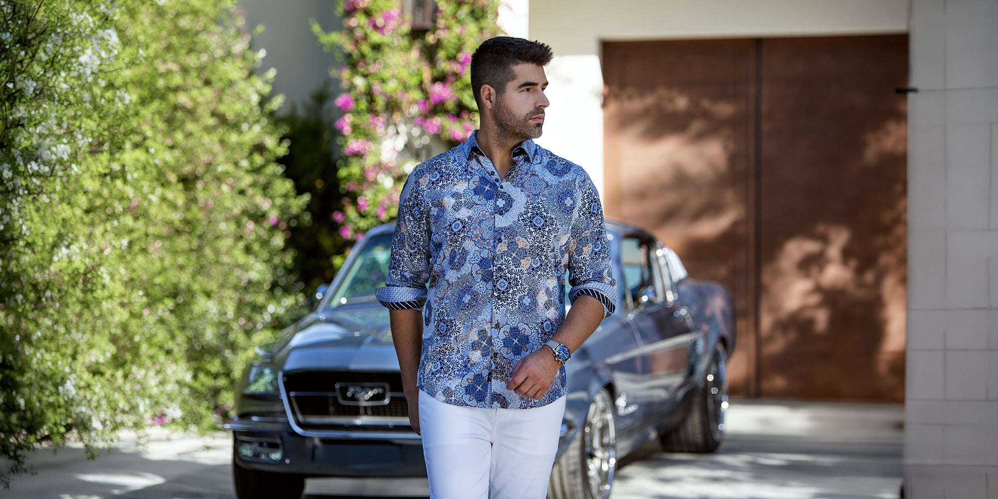Au Noir men’s blue floral dress shirt, styled with white pants in an elegant outdoor setting with a classic car.